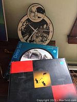 Wall clock close-up showing detailed moon face and whimsical black and white illustration with astronaut, stars, cat, and landscape on table.