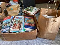 Full view of box filled with assorted vintage maps and travel guides along with a paper bag labeled London/England containing more maps
