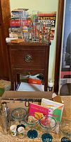 Photo showing cocktail shaker, beer mugs, books on bar and beer making, and various stemware on and around wooden dresser