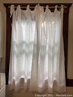 White curtain panels hanging on a window with tie backs and gathered fabric at top.
