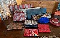 Photo showing a collection of ten women's clutches, wallets, and coin purses in various fabrics and colors arranged on a wooden surface.