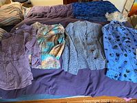 Five women's tops laid flat on a bed showing various colors and styles.