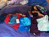 Wide view showing multiple scarves and gloves arranged on a purple surface, displaying variety of colors and textures.