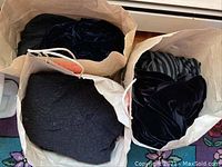 Three paper bags filled with assorted women's clothing items including black, striped, and velvet fabrics