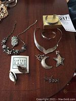 Overview of sterling silver jewelry including necklaces, pins, earrings, and bracelets arranged on a wood surface, showing tarnish.