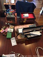 Full lot overview showing jewelry boxes, Olivia pig musical jewelry box, watches, pins and other costume jewelry items arranged on a wood table
