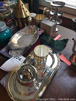 Photo of silver plate serving items on a wooden table, showing large tray, lidded container, oval dish, two-tiered stand, ice cream goblet