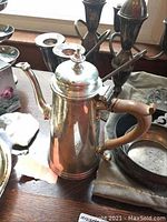 Sterling silver tea/coffee pot with wooden handle in front and two three-arm candlesticks behind on wooden surface