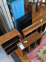 Five CD holders: three wooden racks, one metal rack, and one plastic rack, displayed on wooden floor and rugs.