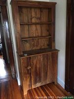 Front view of rustic wooden hutch showing two open shelves on top and a door below with a knob and latch closure.