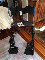 Front view of the foldable mobility chair in rollator configuration on a colorful rug with wooden floors and furniture nearby.