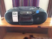 Front view of black Magnavox boom box with large speakers on each side, cassette deck in middle, and control panel on top