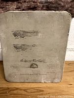 Close-up image of the lithographic stone showing airplane illustrations and company text, highlighting wear and printing details.
