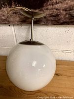 Full view of white globe ceiling fixture with metal mount and hanging rod, resting on wooden surface against wall.