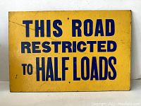 Front view of vintage yellow and blue road sign stating 'THIS ROAD RESTRICTED TO HALF LOADS'.