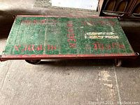 Overall view of wooden flatbed moving cart with green-painted slats and red frame