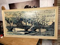 Front view of large framed vintage French art print on a wooden surface with a wall background.