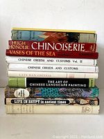 Stack of 11 books, viewed from the side, showing titles including Chinoiserie, Chinese Creeds and Customs Vol II, The Art of Chinese Landscape Painting, and Life in Egypt in Ancient Times.