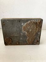 Front and side view of vintage printing block showing tree design carved on metal.