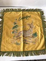 Full view of the yellow square cushion cover with fringe and deer design.