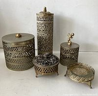 Group photo of five vintage metal vanity containers and tray with detailed cutout designs and finials, showing scale vs a Campbell's soup can.