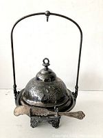 Front view of antique silverplate butter dish with domed lid, handle, and butter knife resting on stand.