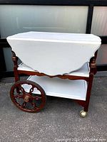 Side view showing white painted drop leaf and large wood wheel on the tea cart with mixed wood and white painted surfaces.