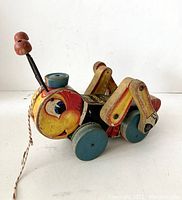 Front angle view of wooden Kriss Kricket pull toy showing face, antennae, wheels, and string.