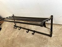 Side view of black metal wall-mounted shelf with horizontal bars and hooks below.