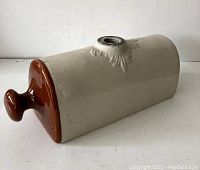 Photo showing the full crock foot warmer, beige ceramic body with brown glazed end and metal capped hole on top.