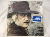 Front cover of Charlie Rich 'Behind Closed Doors' vinyl album showing artist wearing hat and a blue sticker promoting 'The Most Beautiful Girl'