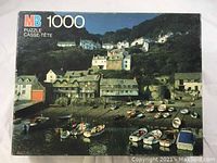 Front of the MB 1000 piece puzzle box showing scenic harbor waterfront image with boats and houses.