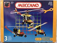 Front of box showing Meccano logo, motor piece, 3 different metal models (helicopter, crane truck, smaller vehicle) possible to build.