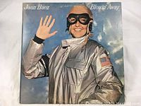 Front cover of Joan Baez's 'Blowin' Away' vinyl LP album showing the artist in a silver aviator suit waving and smiling.