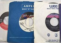 Photo showing three vinyl singles in sleeves, including a Tamla Motown record, an Ampex Music of Canada sleeve, and a Warner/Elektra/Atlantic sleeve featuring a Whitney Houston single.