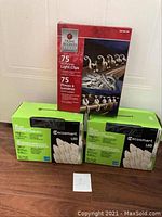 Three boxes stacked: Two Ecosmart green boxes with 50 LED C7 string lights each, one red box of 75 light clips Home Accents brand