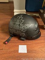 Side view of matte black Rocket motorcycle helmet with skull and piston flaming graphic and red strap buckle