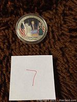 Top view of the commemorative coin in clear capsule on brown textile background with a paper marked 7 beside it.