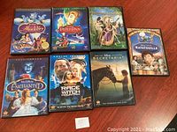 Seven DVDs including Aladdin, Peter Pan, Princess Journals, Ratatouille, Enchanted, Race to Witch Mountain, Secretariat on a wooden surface.