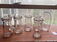 Seven antique milk bottles lined up on a wooden surface with visible slight rosy tint in sunlight.