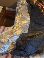 Silver and black motorcycle cover laid out showing the material and size.