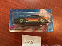 Front angle photo of Hot Wheels Blown Camaro Z-28 diecast car sealed on blue card with light streak graphics. Car is black with red and orange stripes, gold wheels, and engine blower visible on hood. Card has been cut.