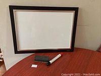 Whiteboard with dark wood frame, dry erase marker and eraser laid out on wooden table