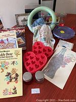 Various crafting books, red silicone molds, glass jars, picture frames, and a large green ring-shaped item on a table