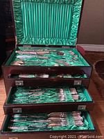 Full view of antique wooden silverware chest with open drawers and green satin lining containing multiple pieces of cutlery.