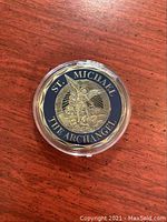Top side of the gold plated St. Michael The Archangel coin in capsule, showing the saint standing over a figure with navy blue and gold lettering.