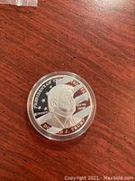 Obverse side of coin showing Donald J. Trump's profile with American flag background.