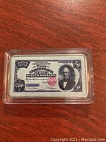 Front view of the silver dollar bar resembling a Fifty Silver Dollars certificate inside a clear protective capsule.