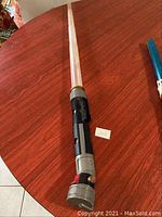 Full view of Star Wars light saber toy laid on a table showing the handle and translucent blade.