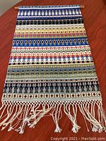 Full view of the wool tapestry showing multiple colorful horizontal rows of guards in various traditional costumes on a wooden mounting rod with fringe.